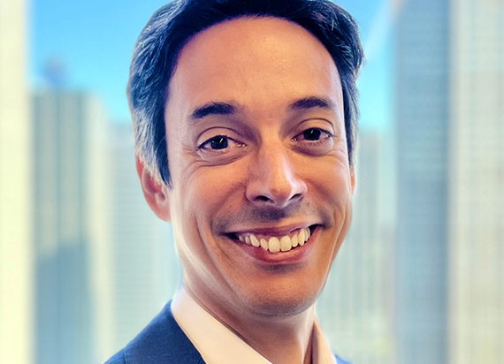 A headshot of Duare Perez smiling with a cityscape background behind him.