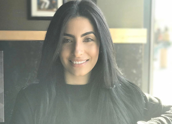 A headshot of Maria Rodriquez taken with a subtle lighting effect among a cafe background.